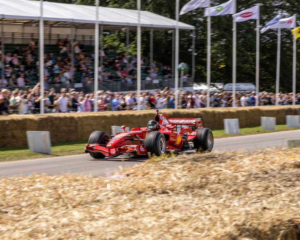 Red race car speeding on track in England with cheering crowd and flags. Vibrant motorsport action.